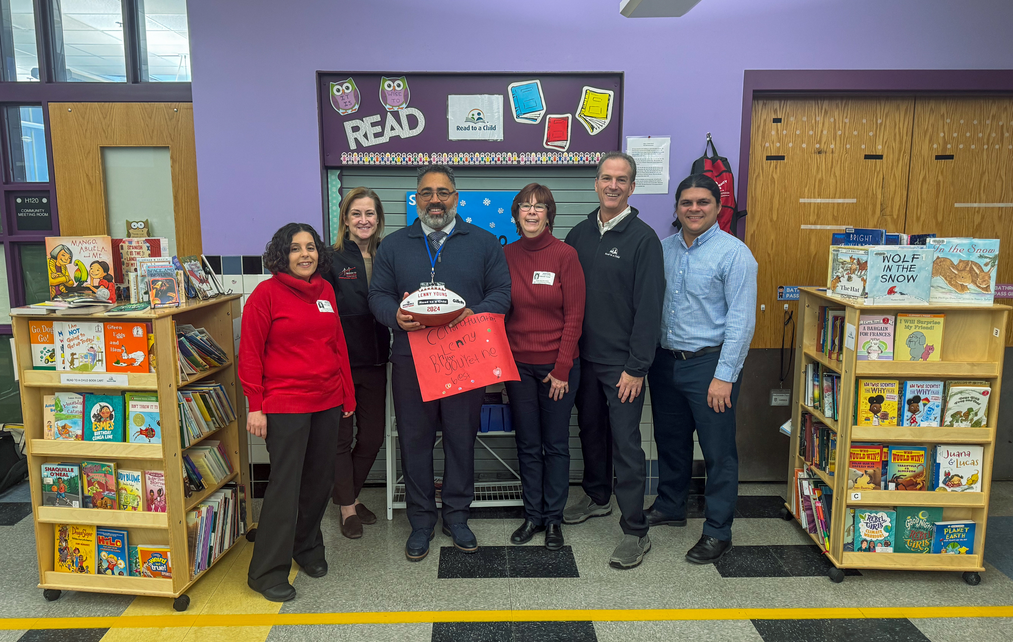 Photo of Hooks School Staff and Read to a Child staff standing between a display of books in an elementary school